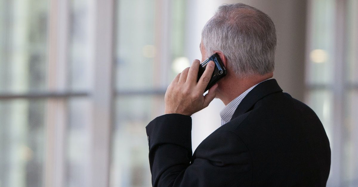 older businessman looking out window while using mobile device